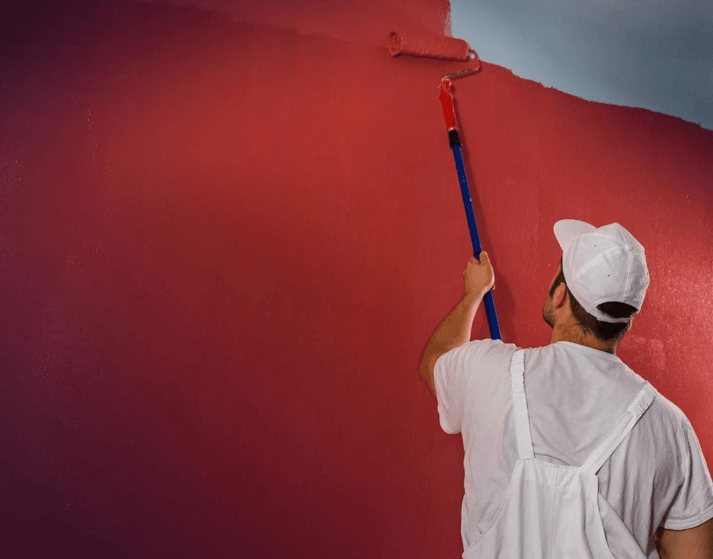 Painter rolling red paint onto an interior wall with an extension pole